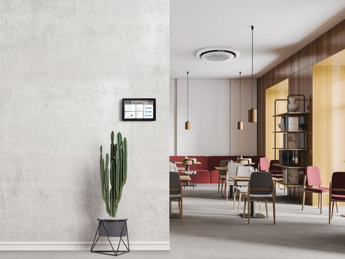 Moderne Büroumgebung mit einem Wandbedienpanel zur Steuerung des Raumklimas, daneben ein Kaktus. Im Hintergrund ist der Samsung 360-Grad-Kassettengerät an der Decke sichtbar | © Samsung